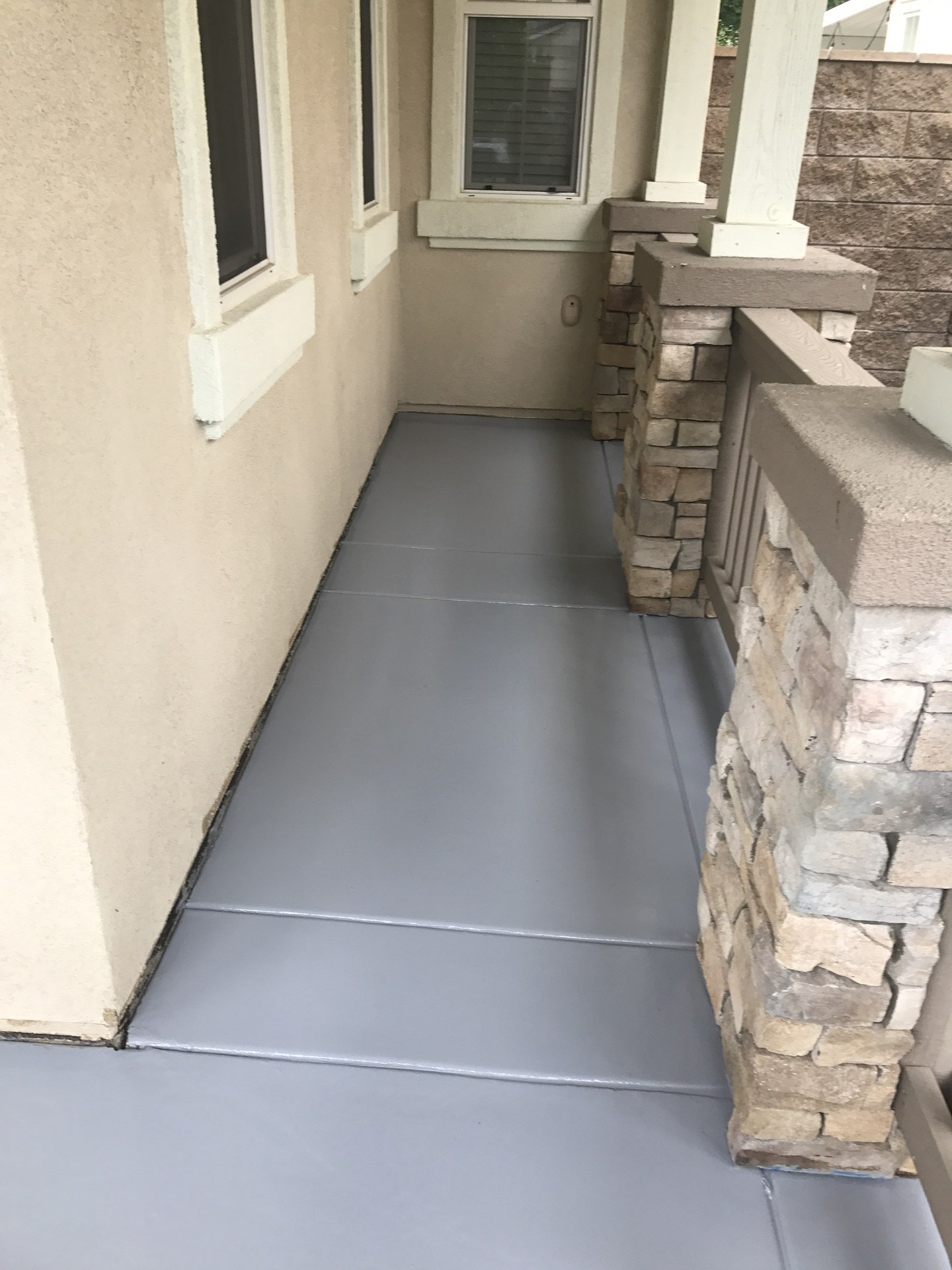 Covered front porch with a solid gray concrete floor coating beside stacked-stone columns