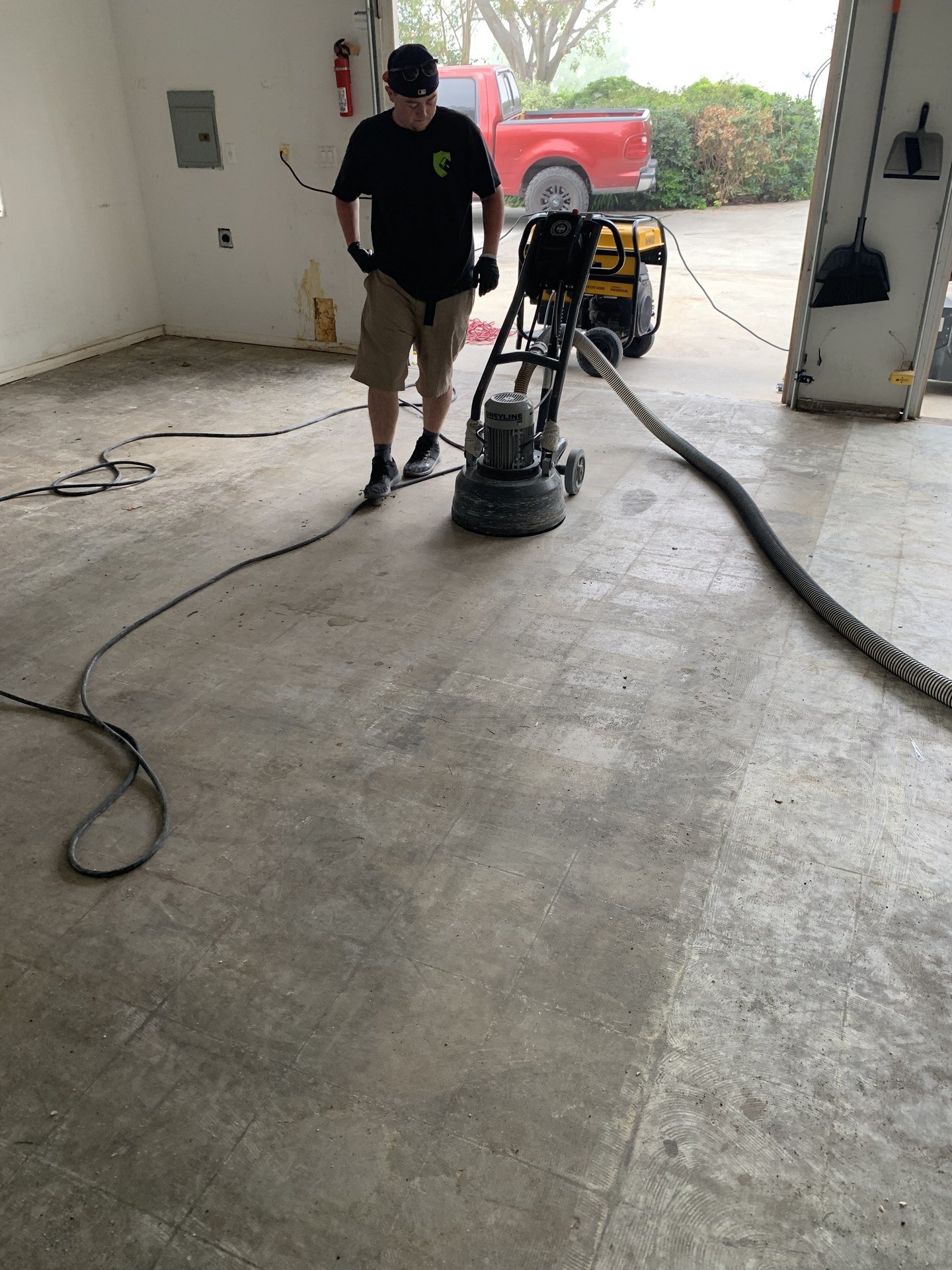 Installer diamond grinding a concrete floor with a dust-extraction vacuum hose attached before coating