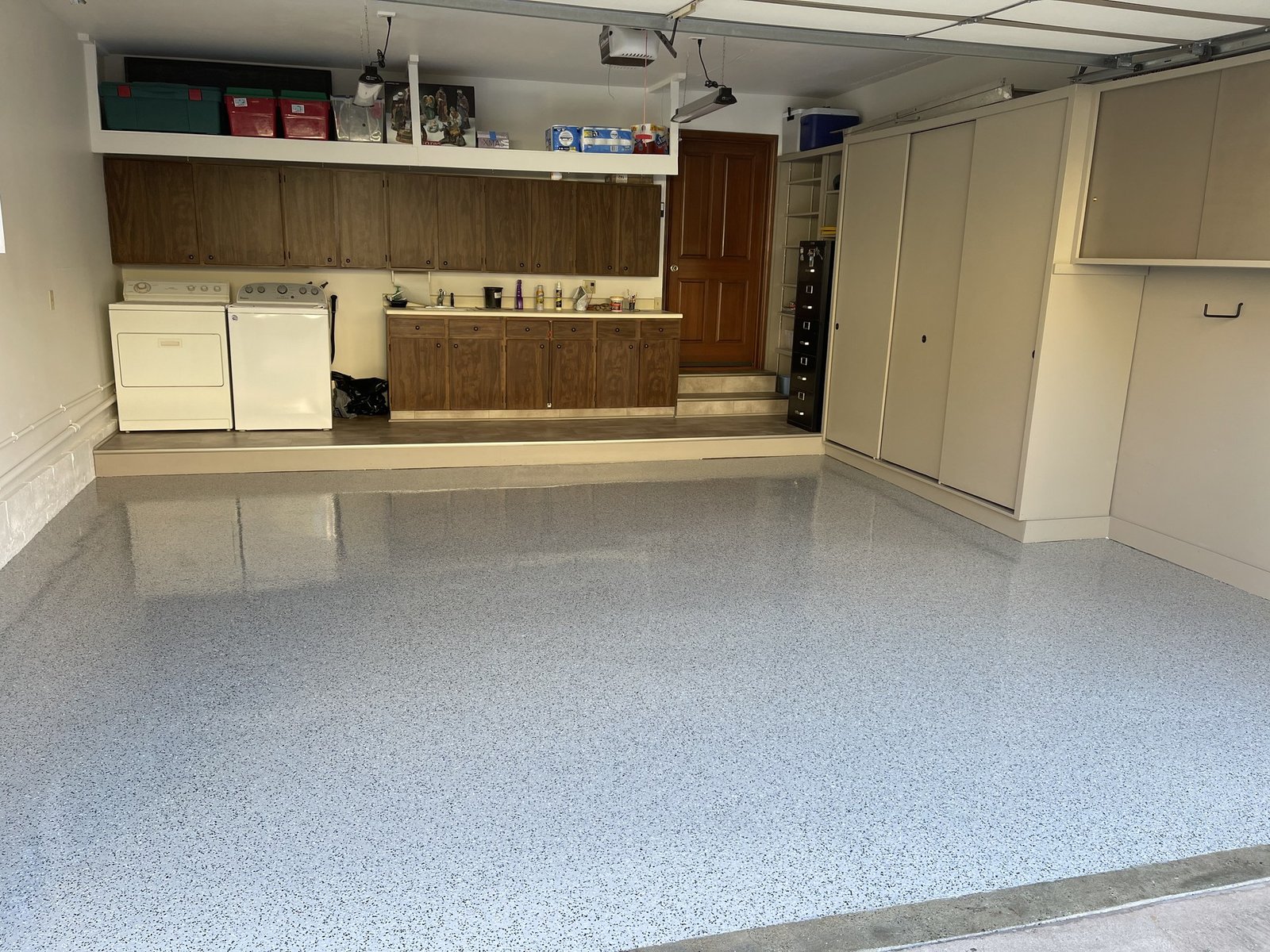 Finished gray flake garage floor coating with a glossy clear topcoat in a two-car garage with built-in cabinets